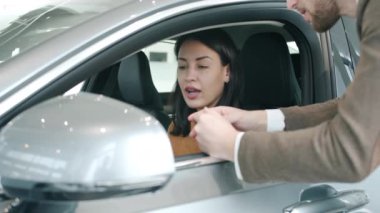 Charming lady talking to car sales manager inside auto in dealership holding controller