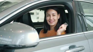 Slow motion portrait of pretty girl smiling inside new car holding keys in dealership