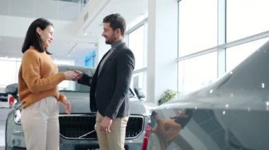 Handsome guy giving car keys to excited woman in dealership hugging smiling
