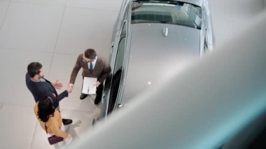 High angle view of young family buying car shaking hands with salesman hugging
