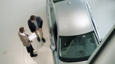 Young businessman talking to car dealer then sitting in automobile in dealership
