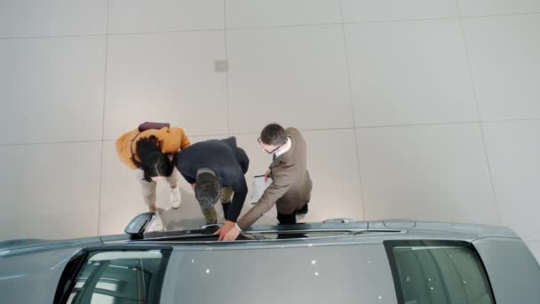 Vista dall'alto della giovane famiglia che sceglie l'auto nello showroom discutendo dell'automobile con il rivenditore — Video Stock
