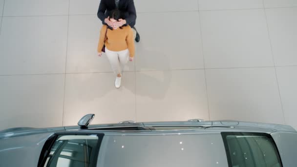 Vista de ángulo alto del hombre dando llaves del coche a la mujer amada como sorpresa en el showroom — Vídeos de Stock