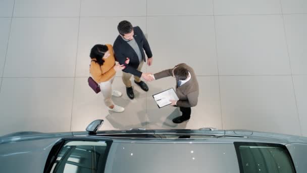 Vista superior de los compradores de coches estrechando la mano con concesionario abrazo en el interior en la concesionaria — Vídeos de Stock