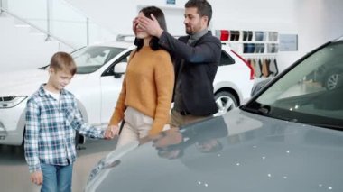 Loving husband and son giving woman car as present making surprise hugging in dealership