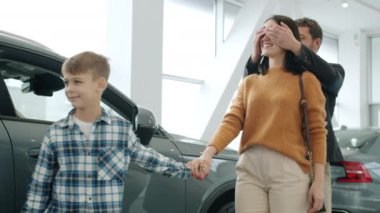 Slow motion of happy woman hugging husband and son getting new car in dealership