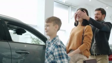 Slow motion of joyful lady getting car as gift from husband and son hugging laughing
