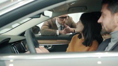 Sales manager talking to young family woman, man and child buying car in dealership