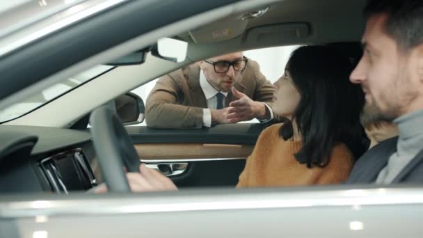 Sales manager talking to young family woman, man and child buying car in dealership — Αρχείο Βίντεο