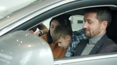 Happy family with adorable kid sitting in car in showroom talking to salesman
