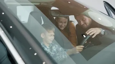 Couple with child in car dealership choosing new automobile while kid holding wheel