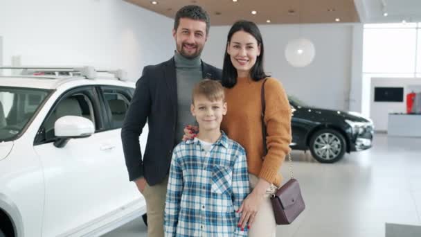 Retrato de mujer feliz de la familia, hombre y niño en la sala de exposición del coche sonriendo mirando a la cámara — Vídeos de Stock