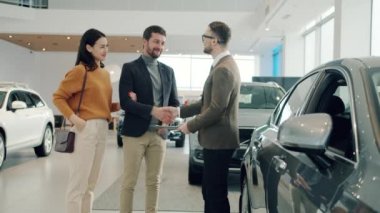 Joyful couple buying car in dealership shaking hands with agent hugging taking keys