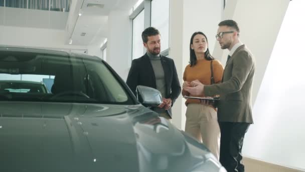 Alegre familia de compra de coches en la concesionaria hablando con el gerente mirando nuevo auto — Vídeos de Stock