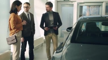 Attractive couple talking to confident car sales manager in luxury car dealership