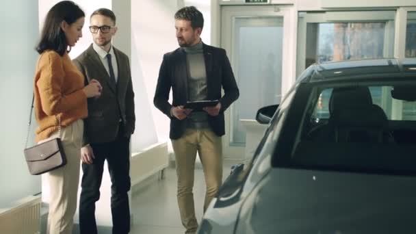 Atractiva pareja hablando con gerente de ventas de automóviles de confianza en concesionario de automóviles de lujo — Vídeos de Stock