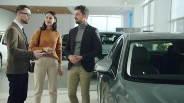 Cheerful husband and wife purchasing vehicle in car dealership talking to manager