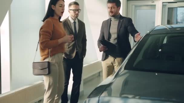 Jovem família marido e mulher escolhendo carro na concessionária falando com o gerente de vendas — Vídeo de Stock