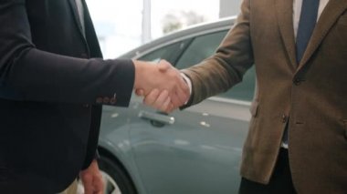 Slow motion close-up of men shaking hands in car showroom taking key fob