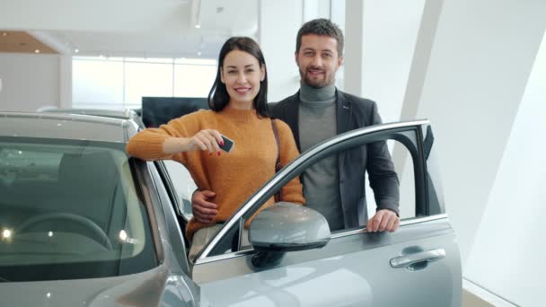 Portrait of man and woman standing near beautiful new car in showroom smiling — Wideo stockowe