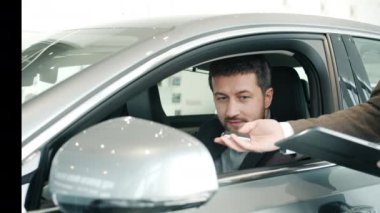Cheerful businessman sitting inside new car testing seat talking to sales manager