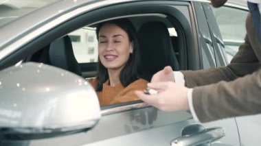 Happy woman getting key fob from salesman in automobile showroom buying car