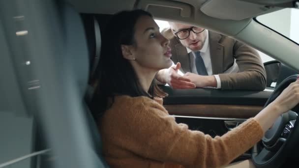 Pretty lady talking to sales representative in motor showroom sitting inside brand new car — Stockvideo