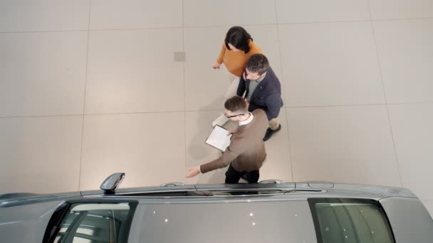 Top view of girl and guy choosing automobile in showroom looking inside talking to dealer — ストック動画