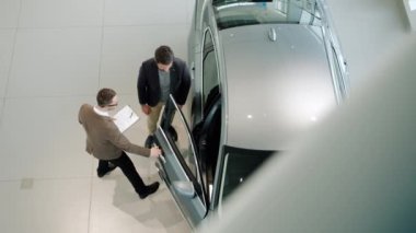 Sales manager opening car door and inviting customer to see the auto inside