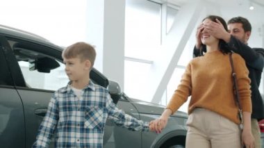 Young family mother, father and child buying car making surprise for woman hugging