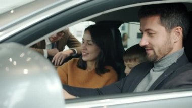 Cheerful people choosing car in showroom talking to manager sitting in automobile