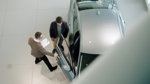 Gerente de ventas abriendo la puerta del coche e invitando al cliente a ver el auto dentro — Vídeo de stock