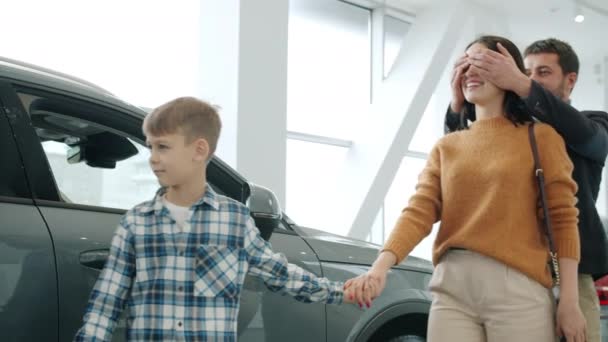 Молодая семья мать, отец и ребенок покупают машину, делая сюрприз для женщины, обнимающей — стоковое видео
