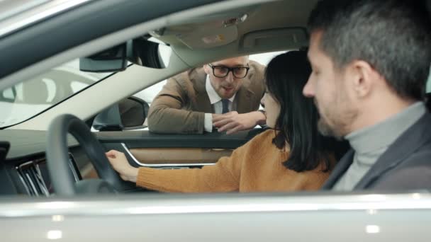 Car dealer selling automobile to young family with child talking laughing in dealership — Stok video