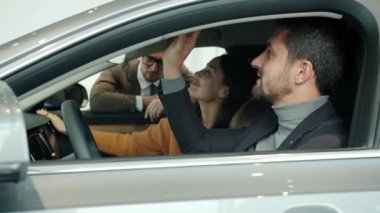 Joyful businessman with wife and son choosing car in showroom talking to sales manager