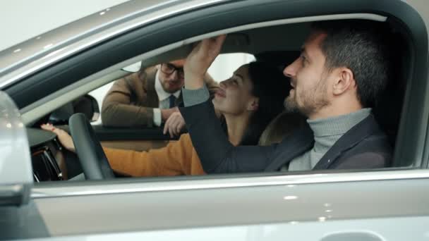 Радостный бизнесмен с женой и сыном выбирают машину в салоне, беседуя с менеджером по продажам — стоковое видео