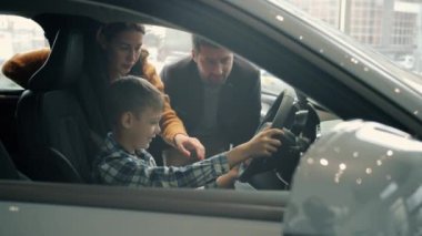 Adorable little kid driving car in dealership buying automobile with parents