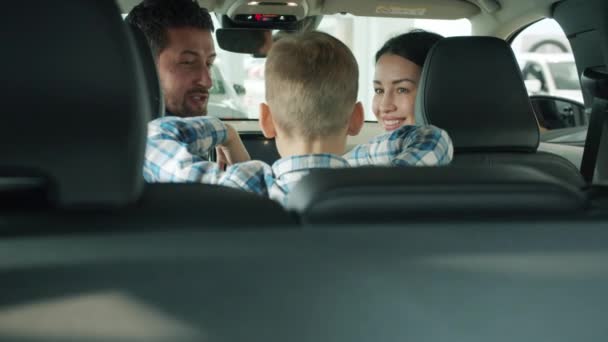 Мать и отец разговаривают с сыном внутри красивой новой машины в автосалоне — стоковое видео