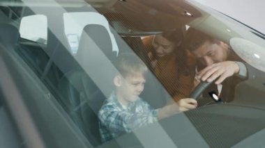 Mother, father and little boy choosing automobile in dealership touching car interior
