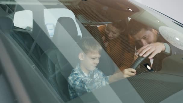 Madre, padre y niño pequeño que elige el automóvil en concesionario tocando el interior del coche — Vídeos de Stock