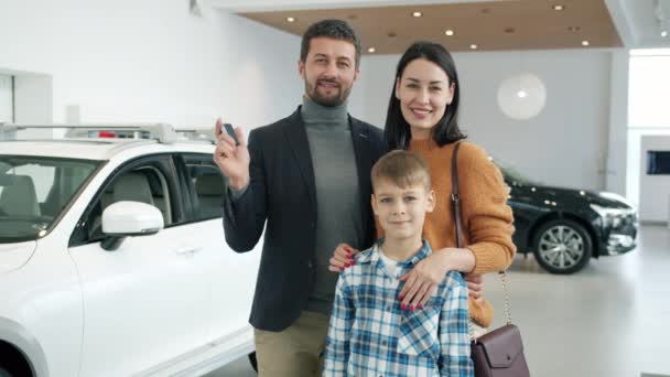 Retrato en cámara lenta de madre, padre e hijo sonriendo en concesionario de automóviles sosteniendo llavero — Vídeos de Stock