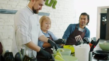 Genç erkek aşçı, öğrenciler öğrenirken sebzeleri fiyonkla karıştırıyor.