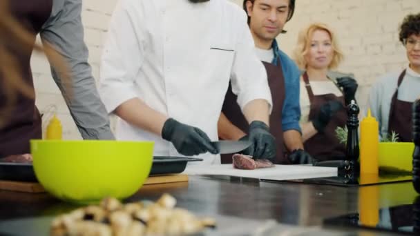 Студенти кулінарної школи спостерігають за шеф-кухарем, який робить м'ясну страву, навчаючись приготуванню їжі — стокове відео