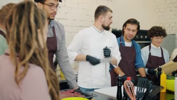 Fešák muž kuchař broušení nůž výuka vaření třídy studentů uvnitř — Stock video