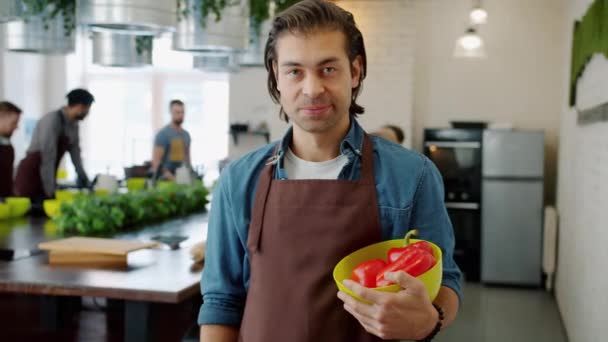 Portrét šťastného muže v zástěře s úsměvem držící misku papriky v kuchařské škole — Stock video