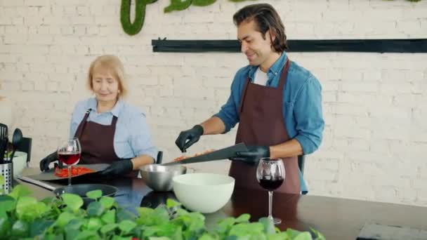 Étudiants de classe de cuisine faisant salade hacher des légumes parler portant des tabliers et des gants — Video