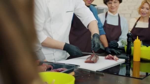 Incline-se de cozinheiro profissional preparando prato de carne na aula de culinária com alunos alegres — Vídeo de Stock