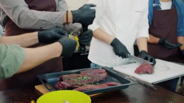 Aşçılar, önlük ve eldiven giyip aşçılığa odaklanmış et yemeği yapıyorlar.