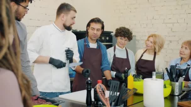 Estudantes da aula de culinária assistindo chef afiar faca na cozinha falando aprendizagem — Vídeo de Stock