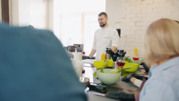 Ung kock undervisning grupp av studenter i matlagning klass prata med leende människor — Stockvideo